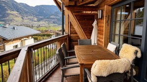 Ein Holzbalkon mit Tisch und Stühlen, mit Blick auf eine gebirgige Landschaft.