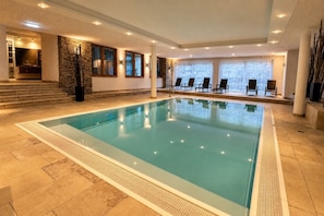 An indoor swimming pool with a tiled floor, stone wall, and multiple windows. - Vrbo Property (Kaprun)