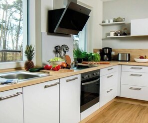 A modern kitchen with white cabinets, a built-in oven, a microwave, and a large window providing a view of trees. - Hohwacht Beach Grove (Hohwacht)