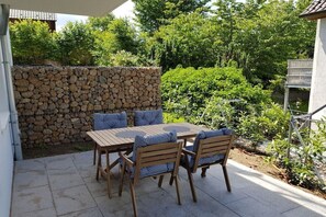 Een terras buiten met een stenen muur, een tafel met stoelen en omliggend groen.
