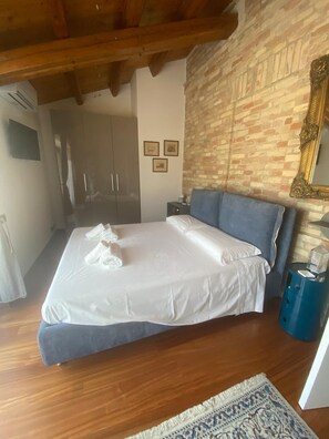 A hotel room with a bed, a blue headboard, a brick wall, and a wooden ceiling. - Relais Infinito: Rooms and Views of the Marche Hills (Montefiore)