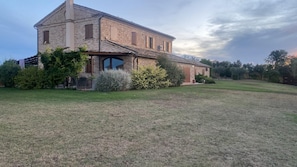 A two-story house with a brick facade, a covered porch, and a well-maintained lawn. - Relais Infinito: Rooms and Views of the Marche Hills (Montefiore)