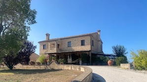 Une maison en pierre à deux étages, dotée d’un porche couvert, d’une allée en gravier et d’un jardin bien entretenu.
