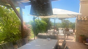 Une terrasse extérieure avec une table et des chaises, une pergola au-dessus et des plantes en pot.