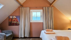 Une chambre avec un plafond en pente, un lit avec des serviettes, une fenêtre avec des rideaux et un tableau accroché au mur.