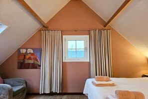 A bedroom with a sloped ceiling, a bed with towels, a window with curtains, and a painting on the wall. - Holiday home in Aagtekerke with Wi-Fi (Aagtekerke)