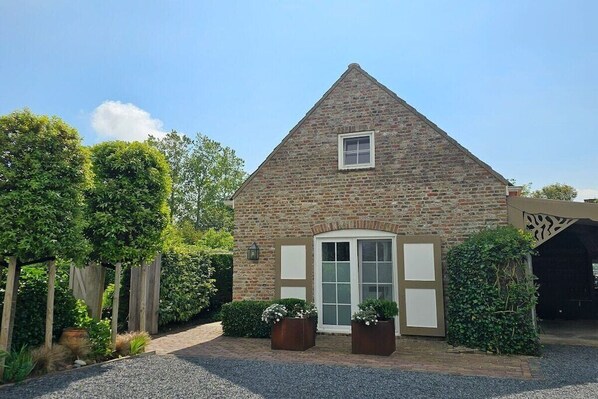 A stone building with a triangular roof, a front door, and two potted plants. - Holiday home in Aagtekerke with Wi-Fi (Aagtekerke)