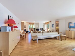 Ett modernt vardagsrum med en soffa, ett soffbord och en tv. På vänster sida står ett träskåp och en röd lampa.