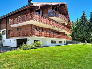 Een houten chalet met meerdere verdiepingen, balkons, een garage en een verzorgd gazon.