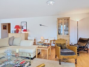 Een woonkamer met een bank, fauteuils, een bijzettafeltje, een schaakbord, een kast met glazen deuren en een lamp.