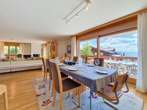 A dining area with a table set for four, large windows with a view, and a cozy seating area with a sofa and chairs. - Résidence Mila n°2 by Interhome (Crans-Montana)
