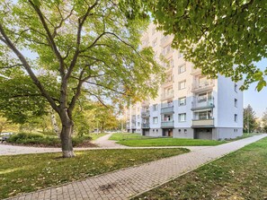 A residential building with multiple balconies, a paved walkway, and a tree in the foreground.