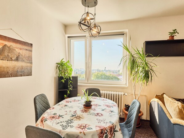 A dining area with a table, chairs, a radiator, and a window with a city view.