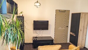 Una sala de estar con un televisor de pantalla plana, un mueble de entretenimiento negro, una puerta con motivos y una planta grande.