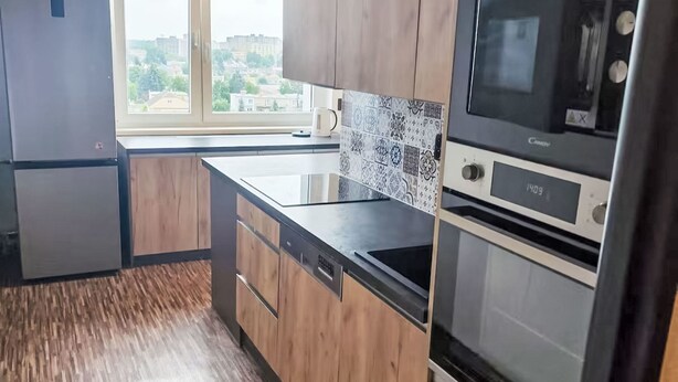 Una cocina moderna con armarios de madera, un refrigerador de acero inoxidable, un horno empotrado y una ventana con vista a la ciudad.