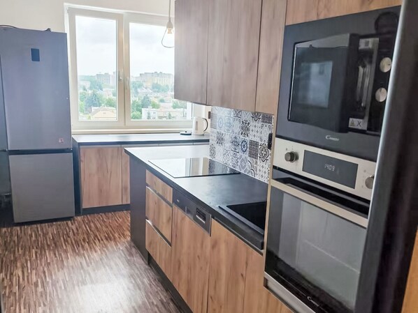 A modern kitchen with wooden cabinets, a stainless steel refrigerator, a built-in oven, and a window with a city view.