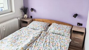 Un dormitorio con colcha estampada, una mesita de noche con lámpara y un cuadro colgado en la pared.