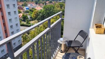 Un balcón con vistas a un paisaje urbano, una mesa con una silla y un pequeño contenedor de madera.
