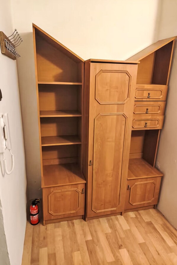 A corner wardrobe with multiple shelves and drawers, a fire extinguisher, and a telephone on the wall.