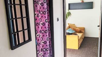 Un vano con un cortinero estampado, una ventana de marco negro y un cuarto con un sofá y una planta.