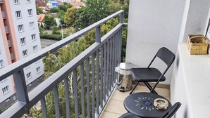 Un balcón con vistas a un paisaje urbano, una pequeña mesa con una silla y un contenedor de madera.
