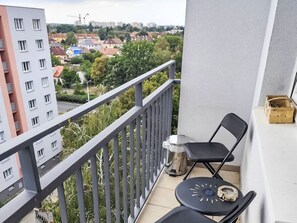 A balcony with a view of a cityscape, a small table with a chair, and a wooden crate.