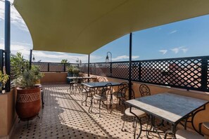 En udendørs terrasse med borde og stole, en stor plantekasse og et dekorativt hegn.