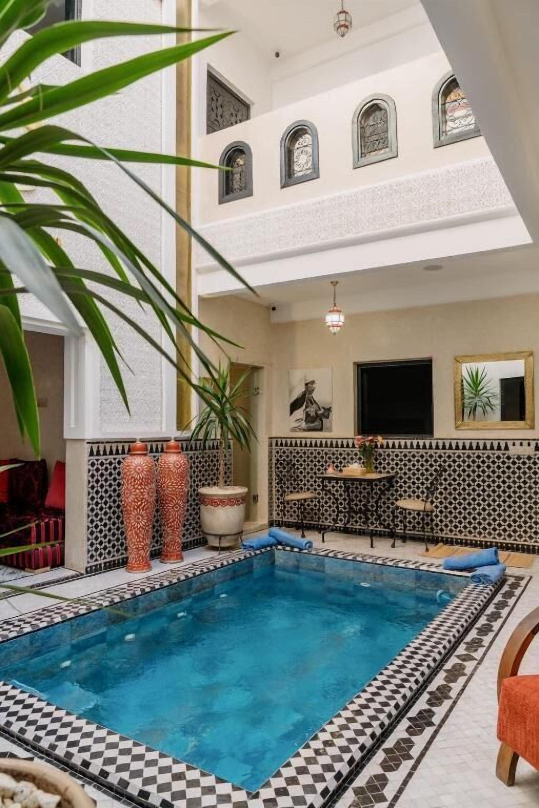 Una piscina interior con un estampado de piso a cuadros, rodeada por una pared de azulejos con diseños geométricos y un techo con ventanales arqueados.