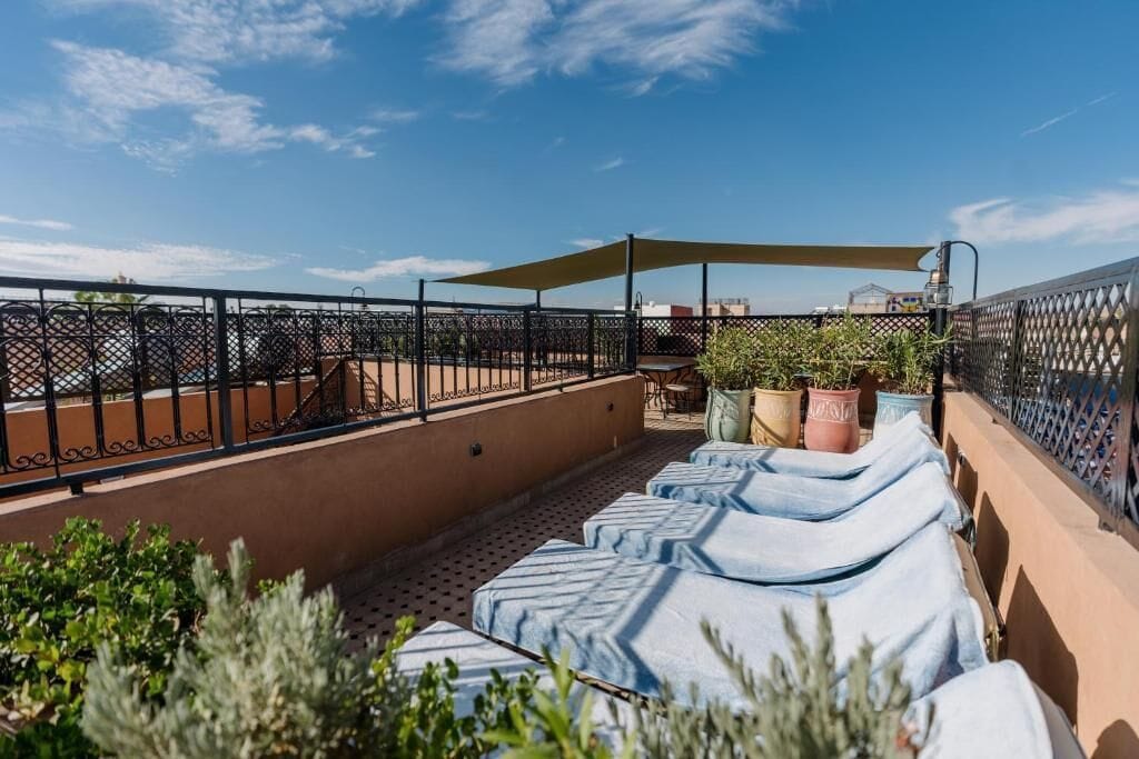 Una terraza en la azotea con sillones, plantas en macetas y una mesa bajo una zona sombreada.