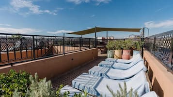 Una terraza en la azotea con sillones, plantas en macetas y una mesa bajo una zona sombreada.