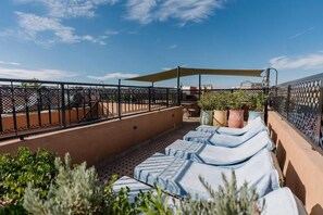 A rooftop terrace with lounge chairs, potted plants, and a table under a shaded area. - Riad Cologne (Marrakech)