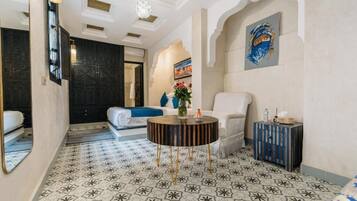Habitación de hotel con piso estampado, una mesita redonda, un sillón blanco y un cuadro en la pared.