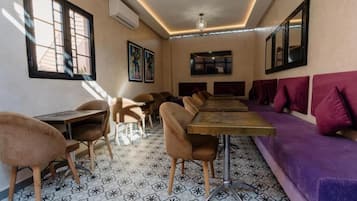 Un área de comedor con una mesa larga y sillas, un sofá morado y baldosas de suelo con diseños.