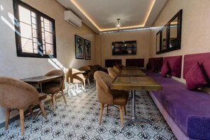 A dining area with a long table and chairs, a purple sofa, and patterned floor tiles. - Riad Cologne (Marrakech)