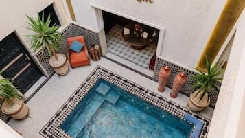 Zona de piscina en la azotea con chimenea, plantas en macetas y el logotipo de 'Riad Cologne' en la pared.