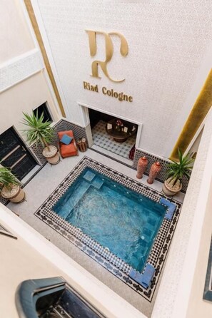 A rooftop pool area with a fireplace, potted plants, and a logo for 'Riad Cologne' on the wall. - Riad Cologne (Marrakech)