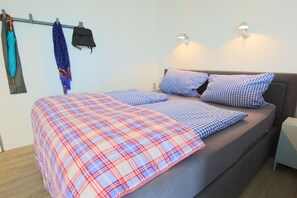 Ein Bett mit einer Karo-Decke und karierten Kissen, eine Wandleuchte und ein Kleiderständer mit Regenschirmen.