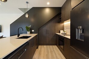 A modern kitchen with a dark wood finish, a stainless steel refrigerator, a dishwasher, and a pendant light. - Prime Location with mountain views (Queenstown)