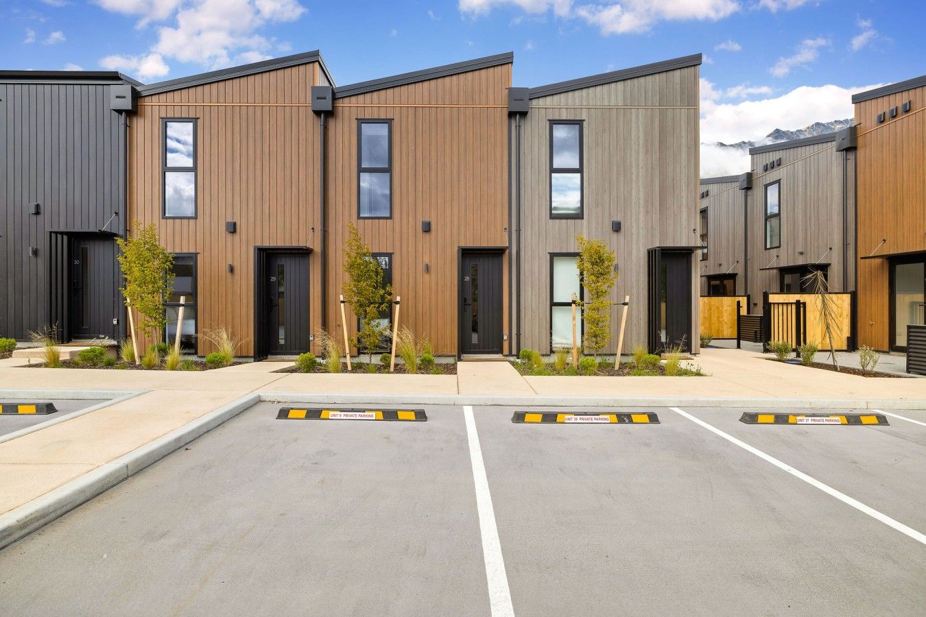 A modern building with multiple units, each featuring a dark-colored entrance and a small garden area.