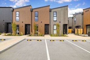 A modern building with multiple units, each featuring a dark-colored entrance and a small garden area. - Prime Location with mountain views (Queenstown)