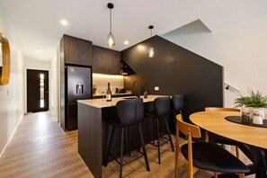 A modern kitchen with dark cabinetry, a central island with bar stools, and pendant lighting. - Prime Location with mountain views (Queenstown)