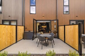 Ein Terrassenbereich im Freien mit Tisch und Stühlen, einem Holzzaun und einem Hauseingang.