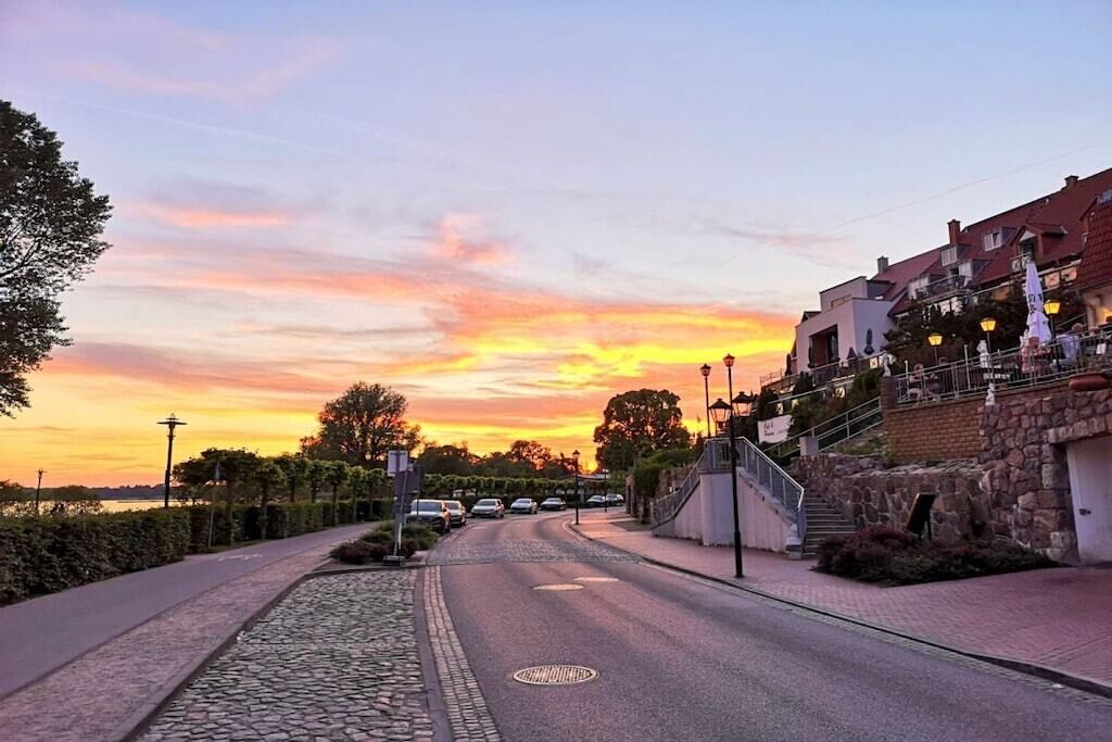 A street at sunset with buildings, a paved walkway, and a stone path.