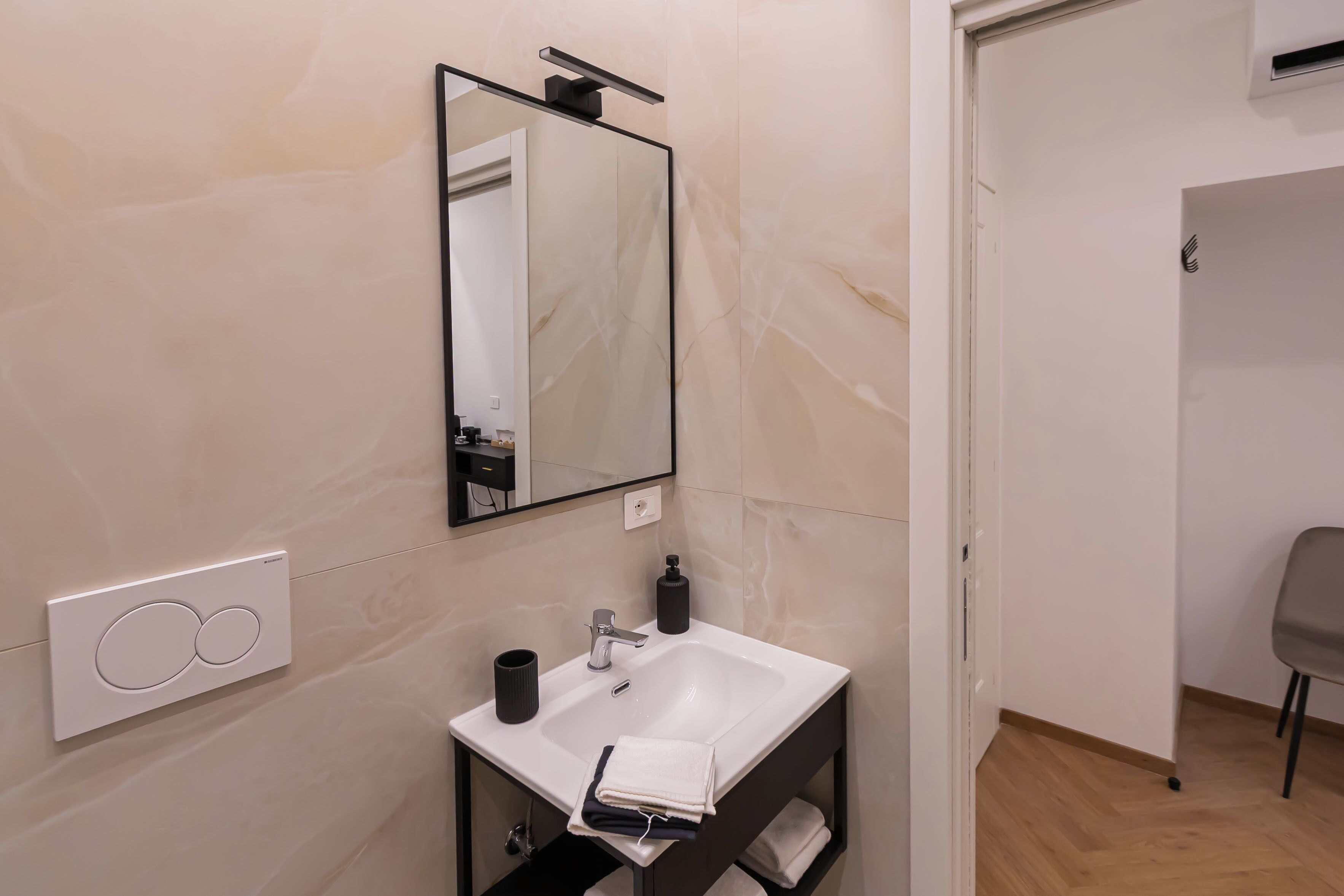 Un baño moderno con un lavamanos blanco, un espejo y un mueble negro.