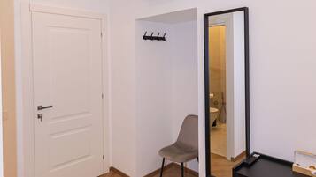 A room with a white door, a black desk with a mirror, a chair, and a black trash bin.