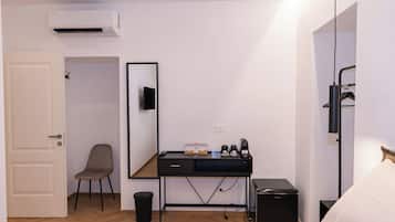 A hotel room with a bed, a desk with a mirror, a chair, a trash bin, and a compact refrigerator.