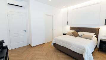 A bedroom with a bed, bedside tables, a desk, and an air conditioning unit.