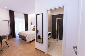 Habitación de hotel moderna con cama, escritorio, silla, espejo y baño con ducha.