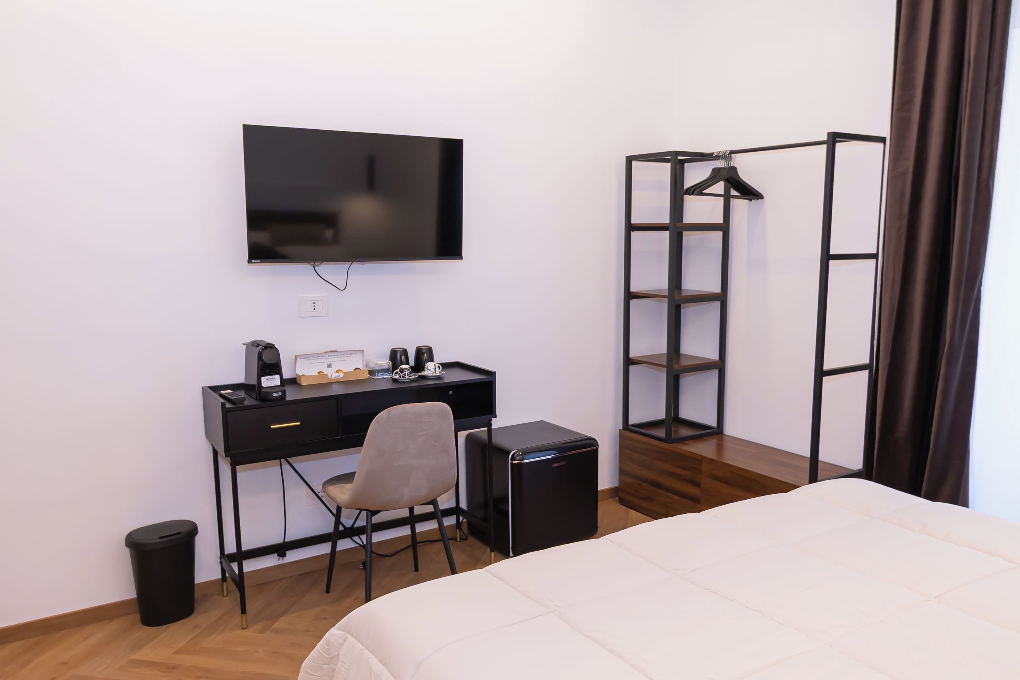 Une chambre d’hôtel comprenant un lit, un bureau avec une chaise, une télévision, un petit haut-parleur noir, une poubelle et une armoire avec un miroir.
