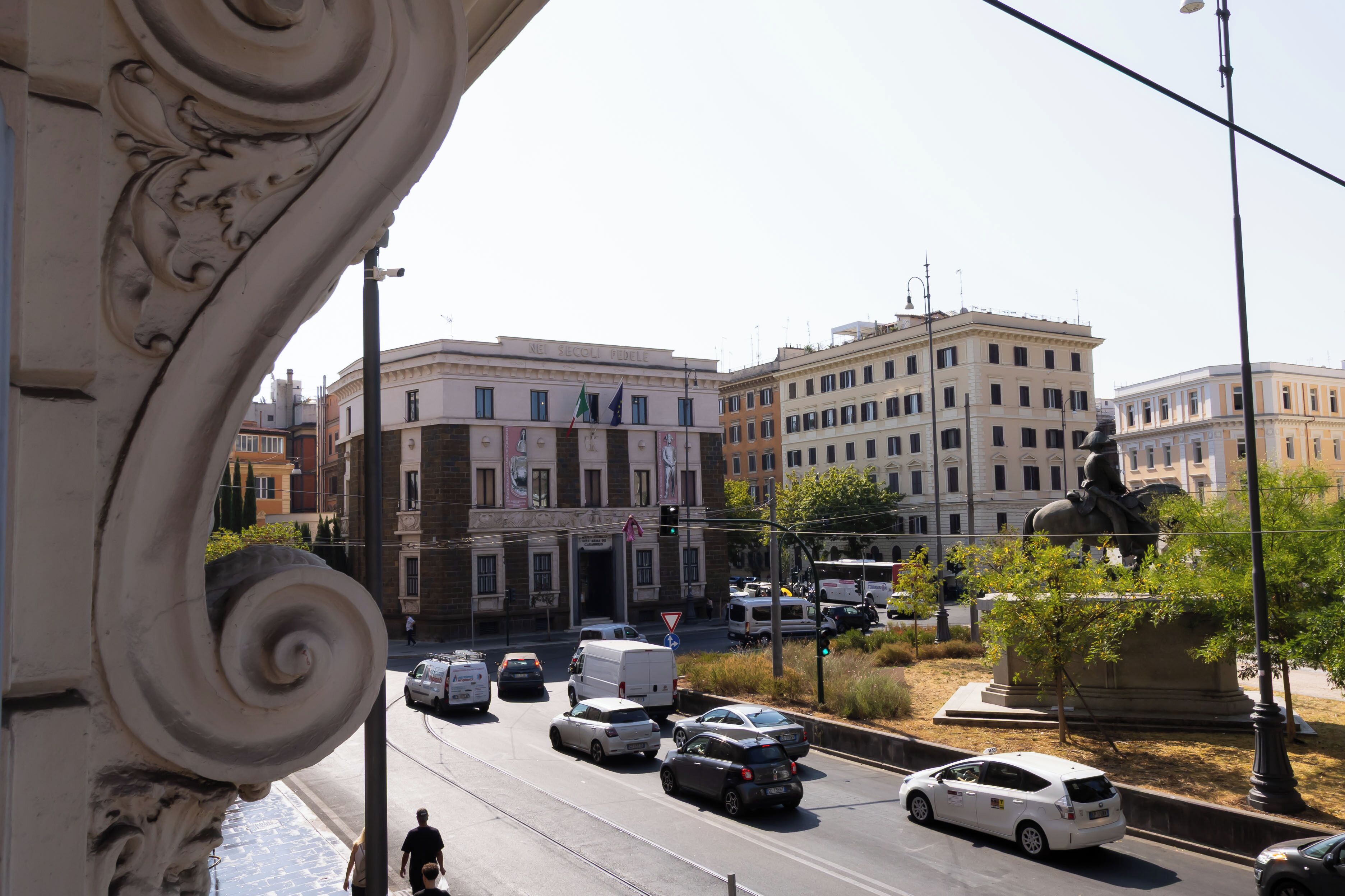 Una vista di strada con edifici, veicoli e una statua.